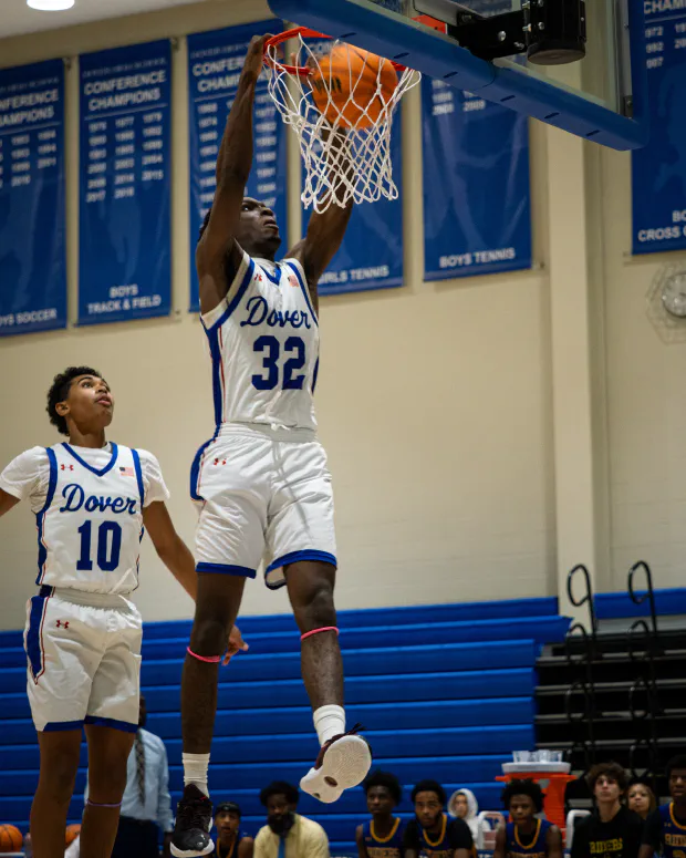 A basketball player hanging from the rim after a dunk, ball still dropping through the net